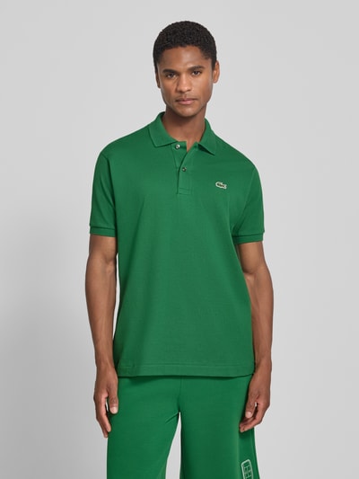 Męski model nosi zieloną koszulkę polo Regular Fit Poloshirt aus reiner Baumwolle model 'CORE' von Lacoste, prosta faktura, Ganzkörperansicht von vorne.