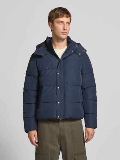 Männermodel trägt Steppjacke mit Kapuze und Reißverschluss von Superdry in Dunkelblau, Regular Fit, Ganzkörperansicht von vorne. Rückenlänge 71 cm, Schulterbreite 50 cm, Brustweite 56 cm, Ärmellänge 83 cm.