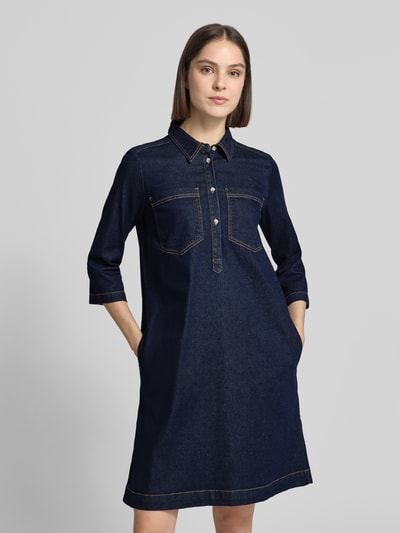 Vrouwenmodel draagt Regular Fit Jeanskleid aus Baumwoll-Mix van Tom Tailor in denimlook met labelpatch, motiefstitching, knielange lengte, hooggesloten hals, knoopsluiting, 3/4-mouw, borstzakken en zijsteekzakken van katoenmix, nahaufnahme bovenlichaam.