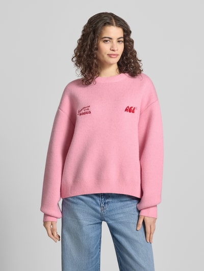 Frauenmodel trägt Relaxed Fit Pullover in Strick-Optik von ANOTHER COTTON LAB, rosa, elastische Abschlüsse, Logo-Stitching, Ganzkörperansicht von vorne.