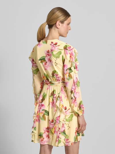 Frauenmodel trägt knielanges Cocktailkleid mit Chiffons und Bindegürtel von V by Vera Mont in Gelb mit Blumenmuster, Volants und tailliertem Schnitt, Allover-Look mit Bindegürtel, Rückenlänge 94 cm, Brustweite 48 cm, Ärmellänge 63 cm, Ganzkörperansicht Rückansicht.