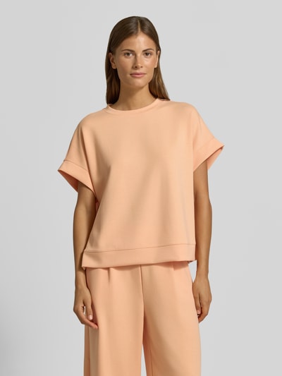 Frauenmodel trägt T-Shirt mit elastischen Abschlüssen von Rich & Royal in Apricot, Relaxed Fit, Modal-Mix mit Stretch-Anteil, Nahaufnahme Oberkörper.
