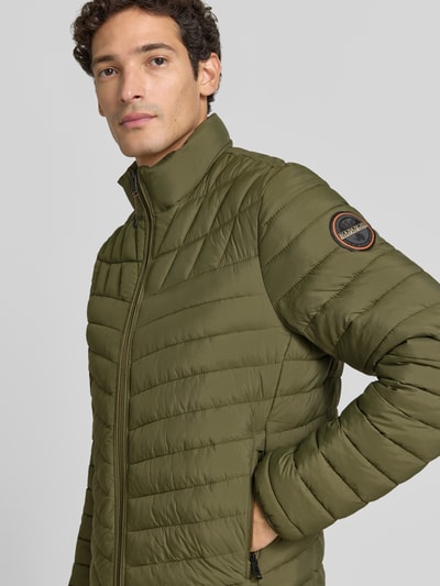 Männermodel trägt Steppjacke mit Label-Patch Modell 'LAPAZ' von Napapijri in Olivgrün, sichtbarer Reißverschluss, Nahaufnahme Oberkörper. Gerader Schnitt, Stehkragen, seitliche Reißverschlusstaschen, sichtbarer Patch, detailreiche Steppstruktur.