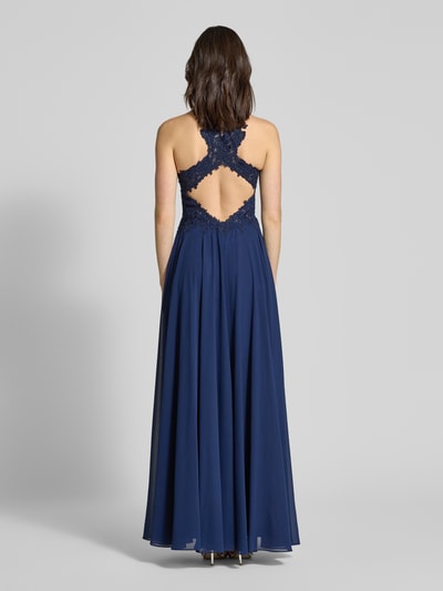 Männermodel trägt Abendkleid mit Rundhalsausschnitt von Mascara w kolorze granatowym, taliaowany krój, ozdobne kamienie, szyfon, dekolt na plecach, długość tyłu w rozmiarze 36: 159 cm, szerokość w rozmiarze 36: 34 cm, widok całej sylwetki z tyłu.