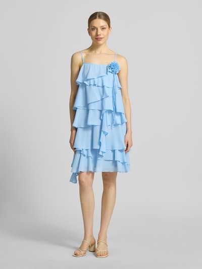 Frauenmodel trägt fließendes Cocktailkleid mit Volants Modell 'ALADYN' von Vero Moda, Optik: Unifarben, Passform: fließend, Mini-Länge, Karree-Ausschnitt, Zierblüte, Trägerform: verstellbare Spaghettiträger, Ganzkörperansicht von vorne.