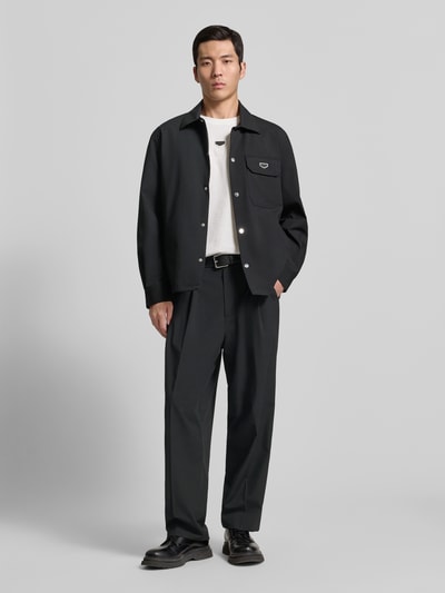 Męski model nosi Stoffhose mit Label-Detail od Antony Morato, czarny kolor, luźny krój, elastyczny pas, widoczne detale, zdjęcie całej sylwetki z przodu. Szerokość w rozmiarze 50: 44 cm, długość nogawki od wewnątrz: 78 cm.