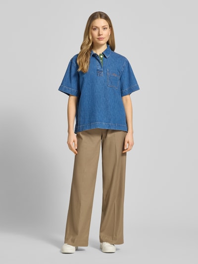 Kobiece model prezentuje Regular Fit Jeansbluse aus reiner Baumwolle od Lacoste, tkanina stylizowana na denim, krój regular fit, kołnierzyk koszulowy, wyhaftowane logo, szwy w kontrastowym kolorze, krótka listwa guzikowa, krótki rękaw, wykończenie z rozcięciami po bokach, brustasza, materiał: czysta bawełna; widok całej sylwetki z przodu