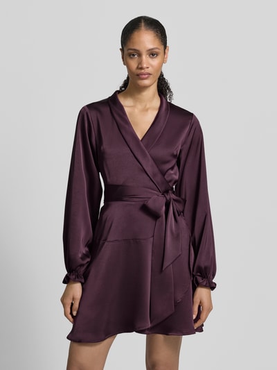 Frauenmodel trägt knielanges Kleid in Wickel-Optik Modell 'Colbie' von Neo Noir aus elastischem Satin, taillierte Passform, langärmelig, mit Taillenband, Rückenlänge 93 cm, Brustweite 48 cm, Ärmellänge 63 cm, Ganzkörperansicht von vorne.