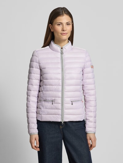 Modelka kobieca nosi Steppjacke mit Reißverschlusstaschen Modell 'SISTER JUDY' von Frieda & Freddies, krój slim fit, stójka, zamek, kieszenie na zamek, długość tyłu w rozmiarze 36: 56 cm, szerokość ramion w rozmiarze 36: 41 cm, szerokość klatki piersiowej w rozmiarze 36: 47 cm, długość rękawa w rozmiarze 36: 61 cm, jasnofioletowa, poziome przeszycia, gładka tekstura, widok całej sylwetki z przodu.