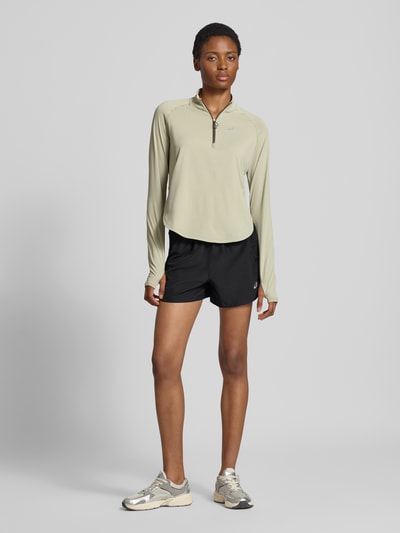 Frauenmodel trägt schwarze Shorts mit elastischem Bund Modell 'NAGINO' von ASICS TIGER, reflektierende Details, gerade Passform, Ganzkörperansicht von vorne.