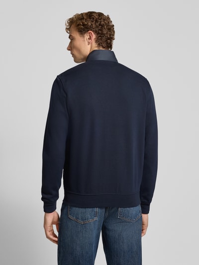 Męski model nosi kurtkę Regular Fit Jacke in Stepp-Optik Model 'Selanik' von bugatti, Mieszanka bawełny, granat, stójka, wpuszczane kieszenie z zamkiem błyskawicznym, zamek błyskawiczny, elastyczne wykończenia, długość tyłu w rozmiarze M: 70 cm, długość rękawów w rozmiarze M: 69 cm, widok całej sylwetki z tyłu.