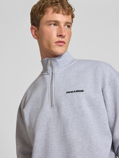 Męski model nosi Relaxed Fit Sweatshirt aus Baumwoll-Mix od PEGADOR, jasnoszary, wyhaftowane logo, ozdobne szwy, długi rękaw, kołnierz zapinany, prążkowane wykończenia, mieszanka bawełny, Ganzkörperansicht z przodu.