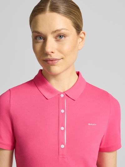Frauenmodel trägt Slim Fit Poloshirt mit Label-Stitching von Gant aus Baumwoll-Elasthan-Mix in Pink, Knopfleiste, Nahaufnahme Oberkörper.