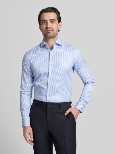 Männermodel trägt Slim Fit Businesshemd aus reiner Baumwolle Modell 'HANK' von BOSS, hellblau gestreift, Haifischkragen, Ganzkörperansicht von vorne.