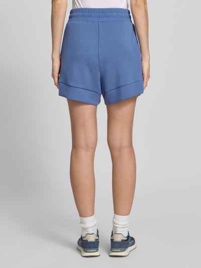 Frauenmodel trägt blaue Shorts mit Eingrifftaschen Modell 'atrium' von VARLEY aus Viskose-Mix mit Stretch-Anteil, Ganzkörperansicht Rückansicht.