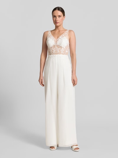 Kobiece model prezentuje Jumpsuit mit Spitze od Laona, krój slim fit, dekolt V, półprzezroczysty, koronka, zamek z tyłu, kremowa biel, gładka tekstura, szerokie nogawki, długość pleców w rozmiarze 36: 54 cm, szerokość w rozmiarze 36: 34 cm, widok całej sylwetki z przodu.