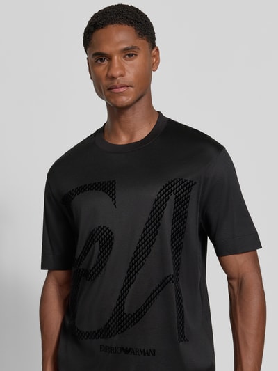 Männermodel trägt schwarzes T-Shirt mit Label-Print von Emporio Armani, Lyocell-Baumwoll-Mix, gerader Schnitt, Nahaufnahme Oberkörper.