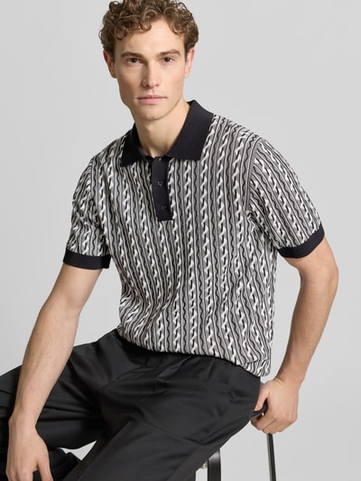 Männermodel trägt Regular Fit Poloshirt mit Polokragen Modell 'Tamian' van Drykorn, katoen, korte knoopsluiting, zwart-wit patroon, Nahaufnahme Oberkörper.