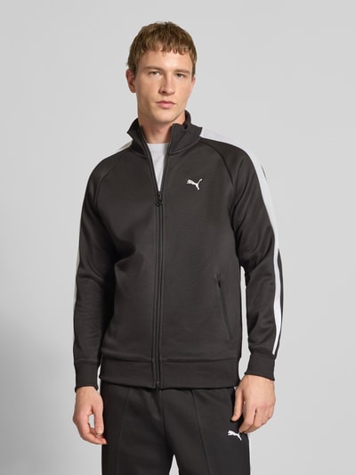 Männermodel trägt Sweatjacke mit Label-Print von PUMA PERFORMANCE in Schwarz mit weißen Details, Material-Mix, Regular-Fit, Gerippte-Abschlüsse, Stehkragen, Reißverschluss, Reißverschlusstaschen, Rückenlänge 73 cm, Ärmellänge 52 cm, Ganzkörperansicht von vorne.
