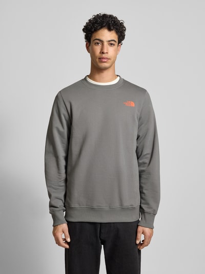 Męski model nosi Sweatshirt mit Label-Print od The North Face z bawełny, krój regular fit, prążkowane wykończenia, okrągły dekolt, nadruk z logo, długość tyłu 69 cm, długość rękawów 72 cm, kolor szary, gładka faktura, całkowity widok z przodu.