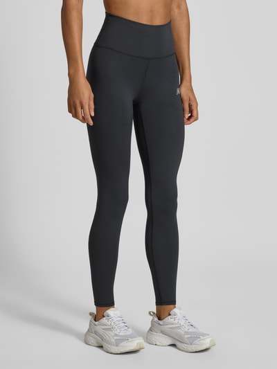 Frauenmodel trägt Leggings mit Label-Print Modell 'Harmony' von New Balance in Schwarz, enger Sitz, elastisch, hoher Bund, Nahaufnahme Unterkörper.