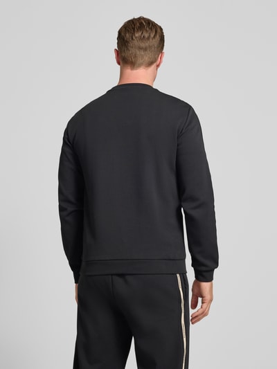 Männermodel trägt Sweatshirt mit Label-Details und Rundhalsausschnitt von EA7 Emporio Armani in Schwarz, Rückenansicht, Baumwoll-Mix, Regular-Fit, Rückenlänge bei Größe M 63 cm, Ärmellänge bei Größe M 66 cm. Ganzkörperansicht Rückansicht.