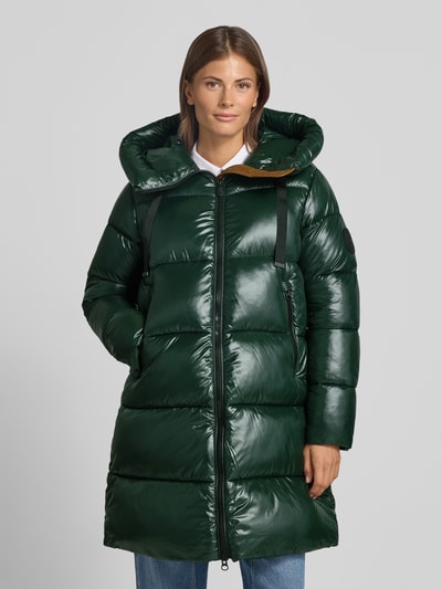 Frauenmodel trägt Steppmantel mit Kapuze und Label-Patch Modell 'ISABEL' von Save The Duck in Dunkelgrün, glänzende Stepp-Optik, Ganzkörperansicht von vorne. Gerader Schnitt, Zweiwege-Reißverschluss, seitliche Reißverschlusstaschen, Tunnelzug an der Kapuze, Rückenlänge 90 cm, Schulterbreite 45 cm, Brustweite 54 cm, Ärmellänge 64 cm.