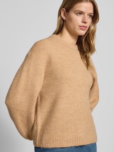 Kobiece model nosi Sweter z dzianiny z dodatkiem wełny od Gina Tricot, luźny krój, prążkowane wykończenia, okrągły dekolt, mieszanka materiałów, długość tyłu 59 cm, długość rękawów 66 cm, jasnobeżowy kolor, widok z przodu do pasa.