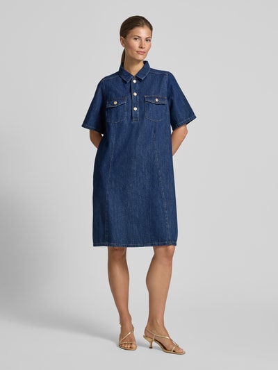Frauenmodel trägt knielanges Jeanskleid mit Brusttaschen Modell 'Biba East' von MOS MOSH in Dunkelblau, reine Baumwolle, gerader Schnitt, Kentkragen, kurze Knopfleiste, strukturierte Jeans-Textur, Ganzkörperansicht von vorne.