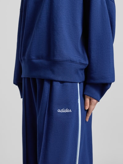 Kobiece modelka nosi Sweatpants mit elastischem Bund od adidas Sportswear, bawełniany miks z wiskozą, luźny krój, haft z logo, zbliżenie na dolną część ciała