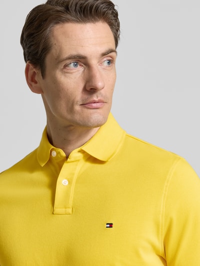 Männermodel trägt Regular Fit Poloshirt aus Baumwoll-Mix von Tommy Hilfiger in Gelb mit Logo-Stitching, Nahaufnahme Oberkörper.