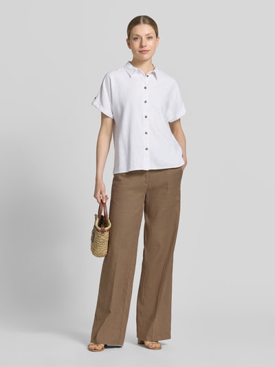 Frauenmodel trägt Relaxed Fit Bluse aus Leinen-Viskose-Mix Modell 'Lava' von FREE/QUENT, weiße Farbe, lockere Form, Knopfleiste, Hemdblusenkragen, kombiniert mit brauner Hose, Struktur und Schnitt der Bluse erkennbar, Ganzkörperansicht von vorne.