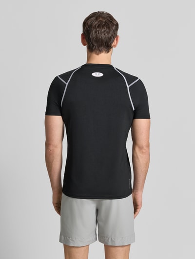 Männermodel trägt T-Shirt mit Logo-Print und Raglanärmel van Under Armour in zwart met witte details, Materiaalmix met stretch, elite fit, ronde hals, ruglengte bij maat M 69 cm, Ganzkörperansicht Rückansicht.