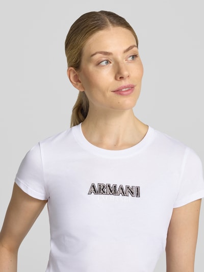 Frauenmodel trägt Slim Fit T-Shirt aus Baumwolle von Armani Exchange, weiß mit Rundhalsausschnitt, Strassstein-Label, Nahaufnahme Oberkörper.