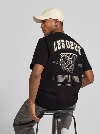 Mężczyznę model nosi czarne T-Shirt mit Label-Print Modell 'Brady whop' von Les Deux z bawełny, prosty krój, nadruk z tyłu, widok z tyłu, Ganzkörperansicht Rückansicht.