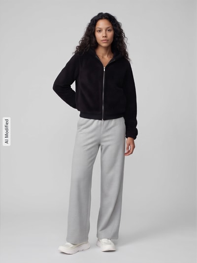 Frauenmodel trägt Regular Fit Sweatjacke mit Kapuze Modell 'NEWANNA' von ONLY, schwarze Jacke und graue Hose, Ganzkörperansicht von vorne, KI-modifiziertes Bild. Damen Sweatjacke von ONLY