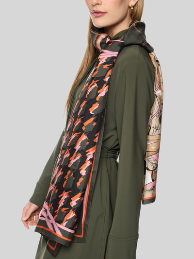 Frauenmodel trägt Seidenschal aus reiner Seide von Marc Cain in Schwarz mit Motiv-Print, eingefasste Abschlüsse, Nahaufnahme Oberkörper.