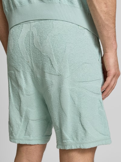Männermodel trägt Regular Fit Sweatshorts aus Baumwoll-Mix Modell 'ASURFER' von BOSS Orange, Optik: Unifarben, Struktur, Label-Patch, elastischer Bundabschluss mit Tunnelzug, Eingrifftaschen, Materialverarbeitung: Frottee, Farbe hellgrün, Struktur-Muster; Ganzkörperansicht Rückansicht.