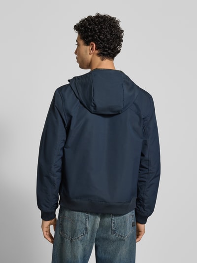 Männermodel trägt Regular fit jack met logoprint model 'Track' van G-Star Raw in donkerblauw, met opstaande kraag, capuchon, steekzakken en elastische boorden, ruglengte maat M 65 cm, schouderbreedte 41 cm, borstwijdte 48 cm, mouwlengte 67 cm, ganzkörperansicht rückansicht.