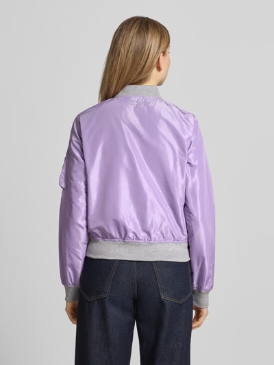 Frauenmodel trägt Bomberjacke mit Label-Patch und Reißverschlusstasche am Ärmel von Original Bombers in Lavendel mit grauen elastischen Abschlüssen, lockerer Schnitt, Rückenansicht, Kontext: Damen Bomberjacke, Stehkragen, Reißverschluss, Logo-Stitching, seitliche Eingrifftaschen mit Druckknopfverschluss, Rückenlänge 53 cm, Schulterbreite 37 cm, Brustweite 48 cm, Ärmellänge 63 cm.