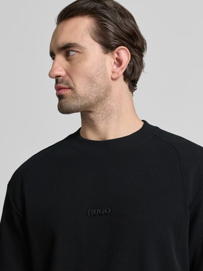 Männermodel trägt Regular Fit T-Shirt aus reiner Baumwolle Modell 'DAFFL' von HUGO in Schwarz mit feiner Struktur, Rundhals, Nahaufnahme Oberkörper.