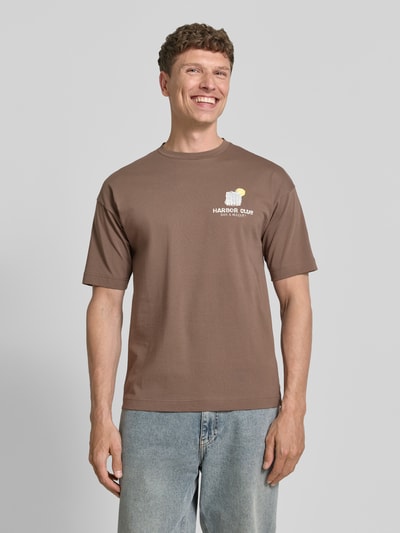 Männermodel trägt T-Shirt mit Motiv-Print und Rundhalsausschnitt von Drykorn in Braun, reine Baumwolle, Regular Fit, Ganzkörperansicht von vorne.