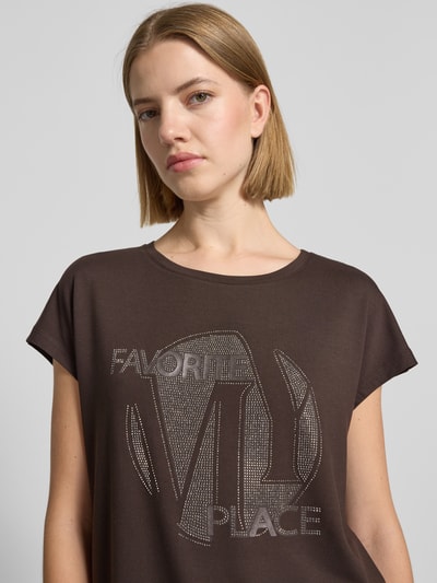 Frauenmodel trägt T-Shirt aus Viskose-Mix mit Ziersteinbesatz von monari in Braun, Regular Fit, Rundhalsausschnitt, Nahaufnahme Oberkörper.