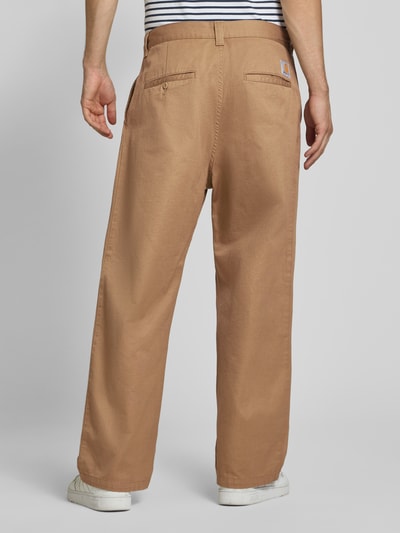 Männermodel trägt Relaxed Fit Stoffhose mit Baumwoll-Anteil Modell 'Brady' von Carhartt Work In Progress in Beige, lockerer Schnitt, Ganzkörperansicht Rückansicht. Material-Mix, Gürtelschlaufen, Eingriff- und Gesäßtaschen.
