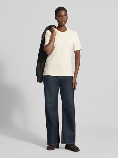 Vrouwenmodel draagt t-shirt met labelstitching van MICHAEL Michael Kors in crème, puur katoen, recht model, ronde hals, ruglengte maat S 65 cm, geheel aanzicht voorzijde.
