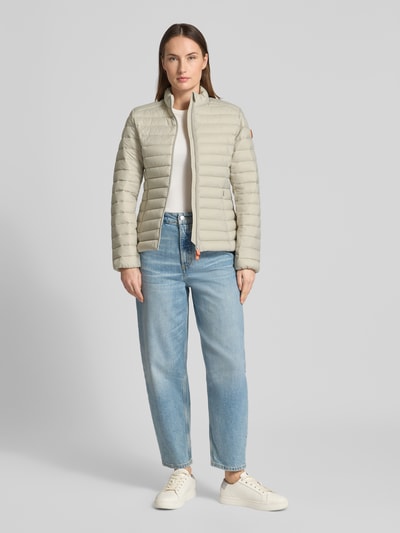 Frauenmodel trägt Slim Fit Steppjacke mit gefüttertem Stehkragen Modell 'Carly' von SAVE THE DUCK in hellem Beige, Stepp-Optik, Ganzkörperansicht von vorne.