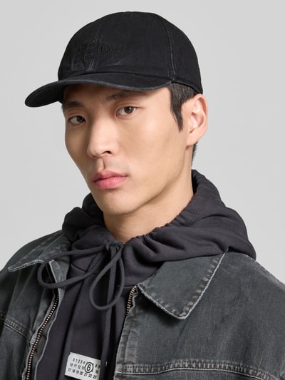 Männermodel trägt Basecap im Used-Look von MM6 Maison Margiela aus schwarzer Baumwolle in Denim-Optik, Label-Stitching, Nahaufnahme Oberkörper.