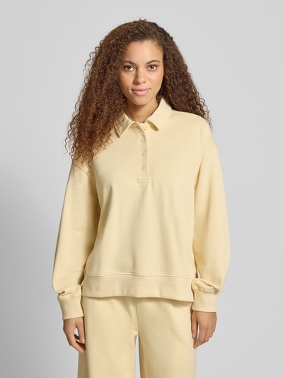Frauenmodel trägt Sweatshirt mit Polokragen und Knopfleiste von Gina Tricot in sanftem Gelb, Regular Fit, überschnittene Schultern, Nahaufnahme Oberkörper.