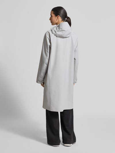 Frauenmodel trägt Mantel mit Zweiwege-Reißverschluss und Kapuze von PEAK PERFORMANCE in Hellgrau, glatte Textur, Ganzkörperansicht Rückansicht. Relaxed Fit, Modell TREELINE HIPE® 2.5L SHELL mit Logo und Kapuze, Maße bei Größe S.