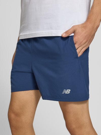 Männermodel trägt Shorts mit elastischem Bund und Logo von New Balance in Blau, Regular Fit, Detailaufnahme Nahaufnahme Oberschenkel.
